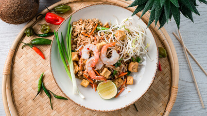 Udon noodles stir fry with shrimp, chicken, carrots, onions, lime, green sprouts and nuts.
