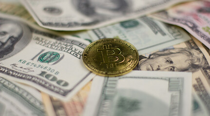 Background, close-up. In a pile of dollar bills in the center lies a coin with a bitcoin cryptocurrency icon. The bitcoin coin is in focus while the surrounding dollar background is blurred.