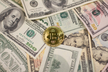 Close-up view from the top. In the center lies a gold-colored bitcoin coin against the background of a solid corve of dollar bills. Bitcoin lies surrounded by dollars. Concept background.