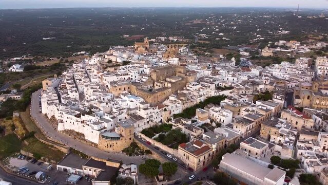 Aerial drone footage of Ostuni - La Citta Bianca (white city), Puglia, Italy at sunset. Establish scene of Cathedral, Porta Nova, the medieval historic old town landmark tourist destination from above