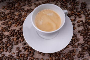 Coffee crema in a white cup with a lot of coffee beans in the background
