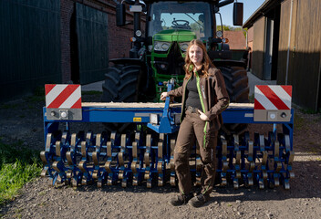 Stolz steht eine junge Landwirtin vor ihren Trecker mit einen landwirtschaftlichen Gerät...