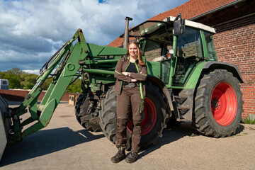 Junge Landwirtin steht vor ihrem Trecker auf den elterlichen Hof.