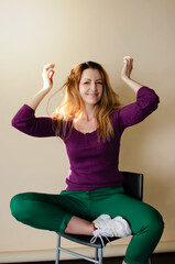 beautiful girl laughs sitting on a chair cross-legged on a beige background