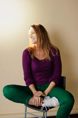 beautiful girl laughs sitting on a chair cross-legged on a beige background