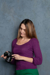 beautiful girl photographer in a purple sweater on a gray background takes pictures. thoughtful girl