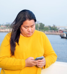 Portrait fat Asian woman long black hair wearing yellow shirt Are using mobile phone or smartphone...