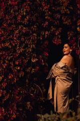 a beautiful sexy brunette woman in a coat by the hedge braided with autumn vines