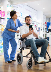 Fototapeta na wymiar Portrait of friendly female pharmacist advising disabled male consumer in wheelchair in pharmacy