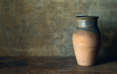 An old clay milk crate. A clay jug without a handle on a wooden table. Vintage water vessel.