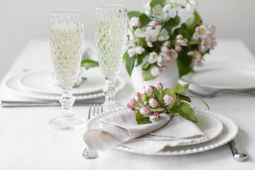 Beautiful table decor for a wedding dinner with a spring blooming apple tree flowers. Celebration of a special event. Fancy white plates, wineglasses