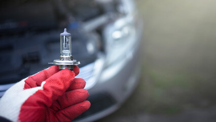 The hand of the master holds a halogen light bulb against the background of the car.Replacing the...