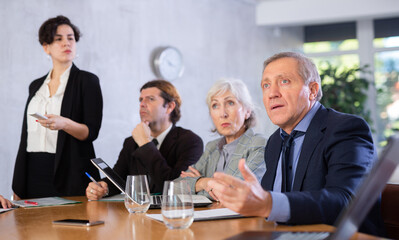 Portrait of surprised elderly businessman sitting at table with colleagues in office and watching presentation during business meeting