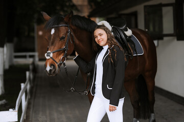 Beautiful professional female jockey standing near horse. woman horse rider is preparing to...