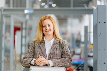 a business woman with long blondes in a plaid jacket stands in the office. 