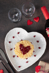Festive puff salad with rice, chicken, eggs and cheese, garnished with pomegranate in heart-shaped plate for Valentine's Day