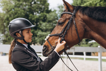 Beautiful professional female jockey standing near horse. Woman horse rider is preparing to equitation
