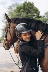 Woman standing near horse. Rider in a black uniform, wearing helmet