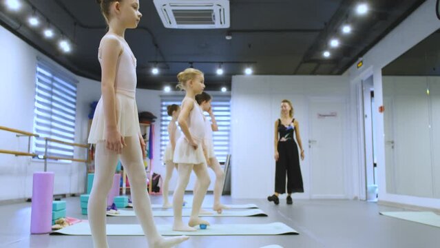the teacher watches how the girls do the warm-up of the feet in the ballet class