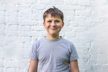 A funny boy smiles intensely against the background of a brick wall. A happy emotional teenager.
