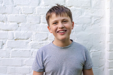 A satisfied teenager with a smile with teeth against the background of a brick wall