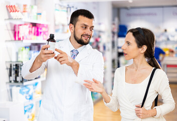 Fototapeta na wymiar Friendly man pharmacist helping young adult woman choosing medical supplies at drugstore