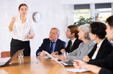 Confident interested young businesswoman doing presentation to colleagues during work meeting in...