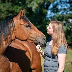 Reiterin und Pferd schauen sich direkt in die Augen auf einer Koppel.