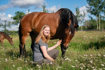 Junge Frau kniet auf einer Weide neben ihrem Pferd.