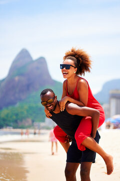 young black brazilian carioca couple in piggyback position smiling and having fun in Ipanema beach Brazil
