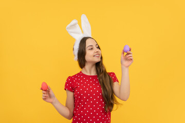 Portrait of teenage girl child wearing bunny ears holding easter eggs isolated at yellow background.