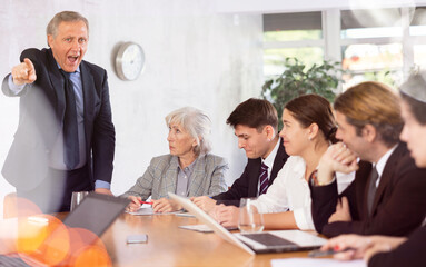 Dissatisfied senior manager reprimanding subordinates due to unfulfilled tasks sitting at table...