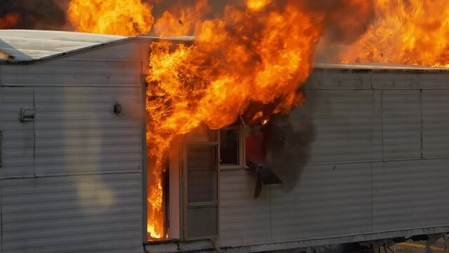 4K Close up detailed shot of large flames billowing from a small building. Real footage of a trailer home on fire.