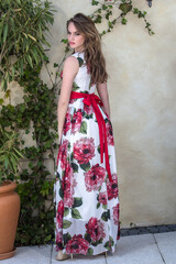 Girl in a summer dress stands next to a flower wall