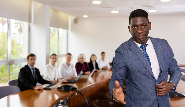 Portrait of positive african-american man in suit offering a handhsake and looking at camera. Friendly businessman in meeting room.