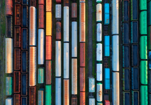 Aerial view of freight trains at sunset. Colorful railway cargo wagons with goods on railroad. Drone view of colorful wagons. Depot of freight trains. Railway station. Heavy industry. Transportation