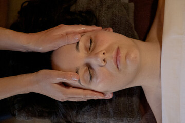 Two hands of a masseuse massaging the head from above