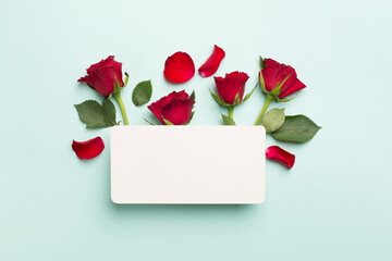 Greeting card mockup with red roses on color background, top view