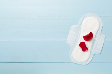 Menstrual pad with red petals on wooden background, top view