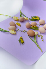 bright composition of chiken eggs and yellow tulips on a purple background