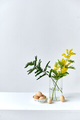 spring arrangement of flowers in a  glass flask and chicken eggs next to it. Minimalism. Easter concept
