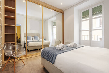 A double bedroom with a large wardrobe covering one wall with oak wood edged sliding mirror doors