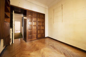 Obraz premium An old and empty bedroom with a built in wardrobe with two folding doors with dark wooden paneling