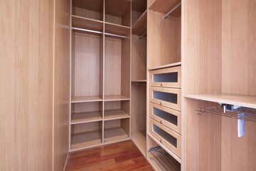 Interior of an empty walk-in closet with drawers, hangers, bars for hanging clothes and a number of shelves
