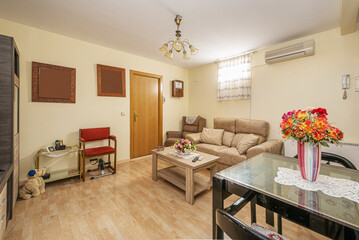 A living room furnished with a beige sofa, a square black wood and glass dining table and matching chairs, laminated flooring and oak doors