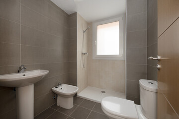 A bathroom with a simple design with its four white porcelain toilets and brown tiles with an oak door