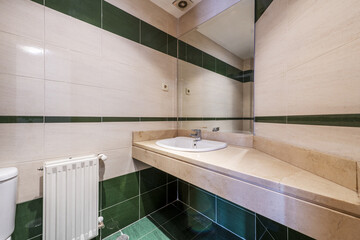 Bathroom with chunky cream marble countertop with white porcelain inset sink under frameless mirror and green tiled flooring