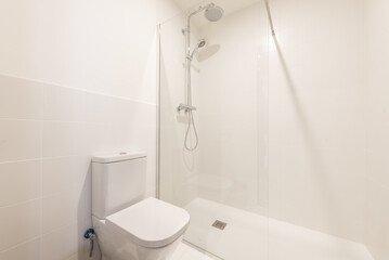A simple bathroom with a porcelain toilet and a glass-enclosed shower stall with chrome faucets and...