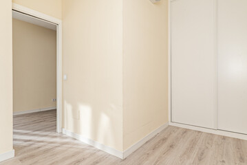 Fototapeta na wymiar Empty bedroom with white wooden sliding door wardrobe on one wall, smooth yellow cream painted walls and laminate flooring