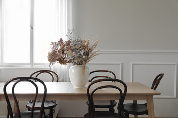 Elegant dining room, scandinavian interior. Vase with dry flowers on wooden table. Vintage chairs. White wall moulding background, stucco decor and window. Empty copy space. Elegant flat, home. - obrazy, fototapety, plakaty